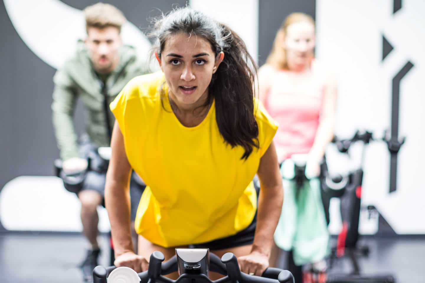 A girl wearing a vibrant yellow tshirt is motivated in an indoor cycling class. goal-setting, success, GamePlan A, confidence