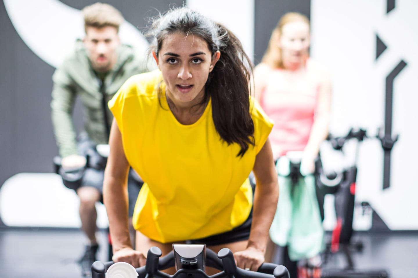 A girl wearing a vibrant yellow tshirt is motivated in an indoor cycling class. goal-setting, success, GamePlan A, confidence