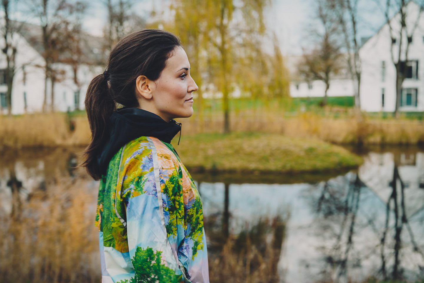 A woman wearing fitness clothing stands by a pond on a cold day. outdoors, environment, calming, peaceful.
