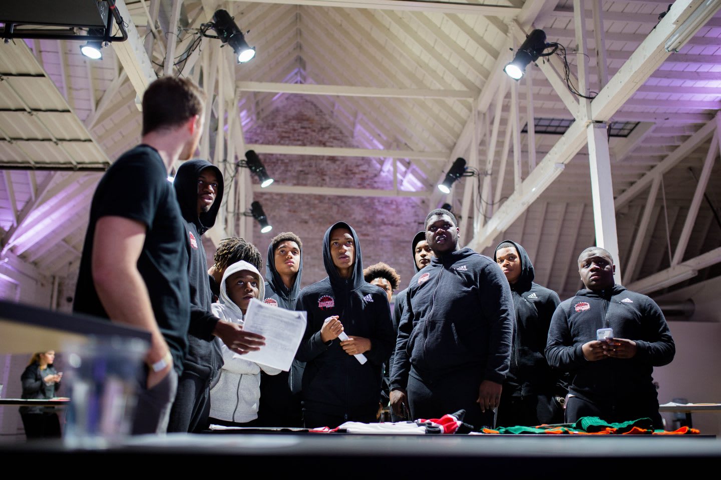 A group of people stand still in curiosity while taking part in a workshop in a warehouse type building. collaboration, collaborate, teamwork, learning