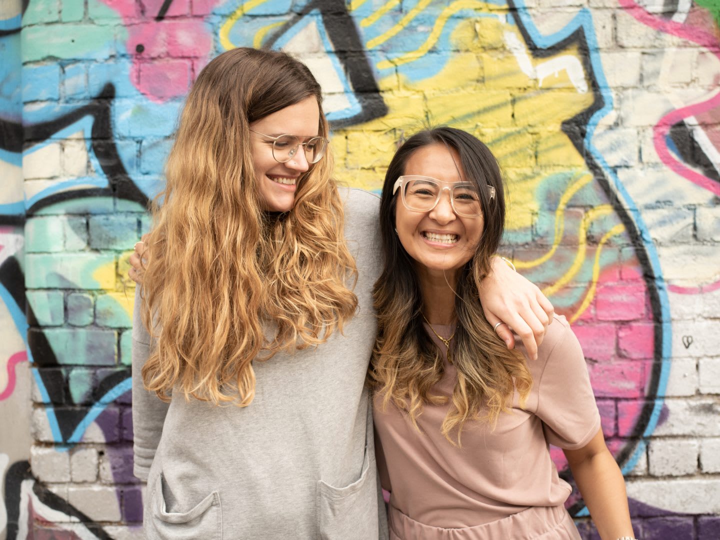 Two friends wrap an arm around each other smiling. friends, smiling, happy, graffiti