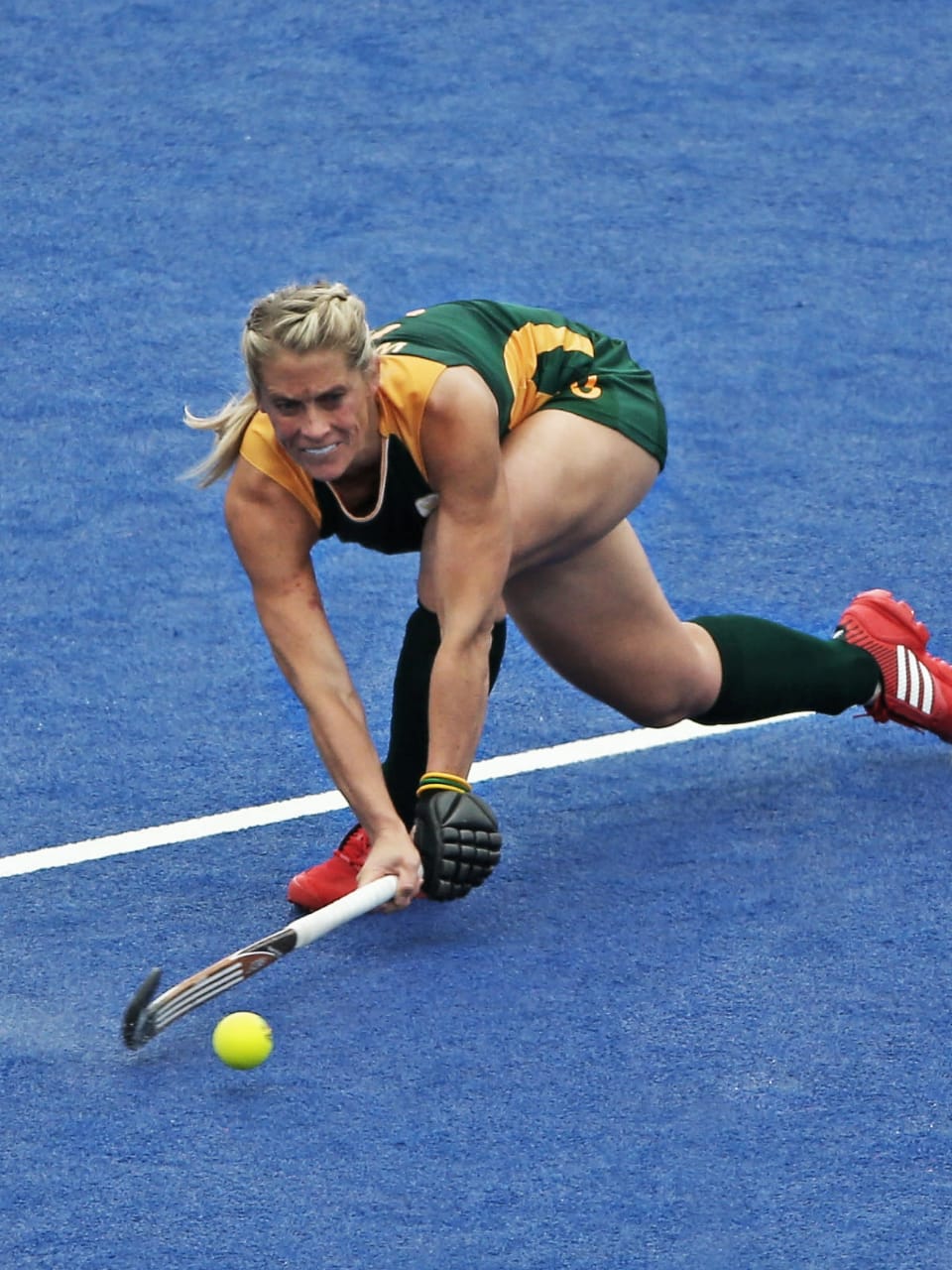 : Kate Woods is playing the ball during a field hockey game wearing the jersey of the South Africa national team.