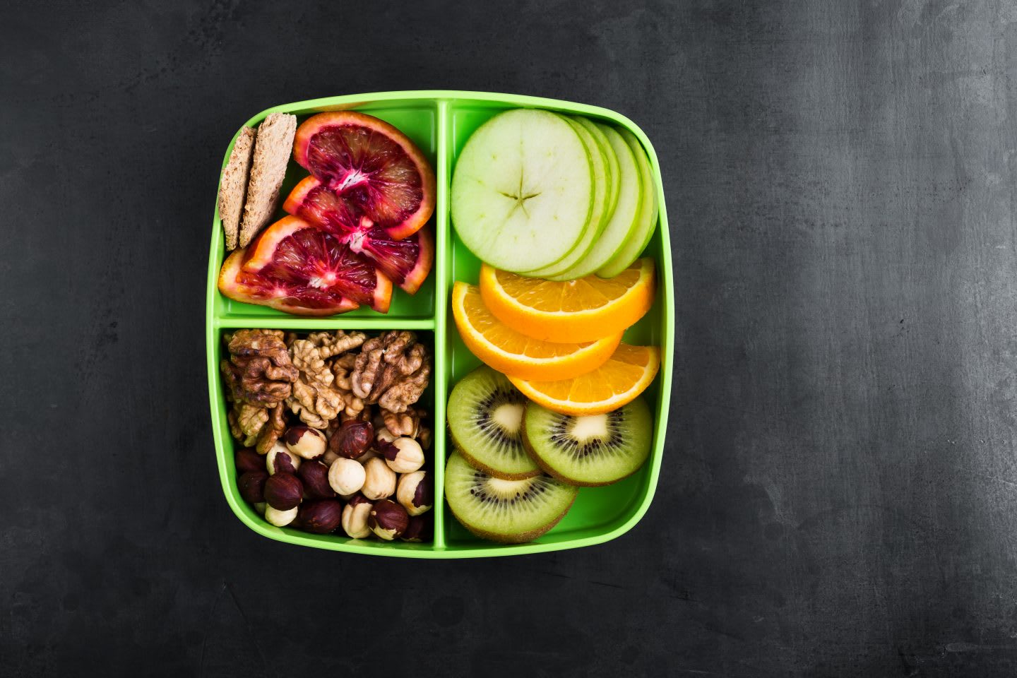 Healthy fruits and nuts snack box with oranges, apples, kiwi,walnuts, hazelnuts, and crackers viewed from above. nutrition tips, healthy nutrition, fitness, outdoor, hiking, food, GamePlan A