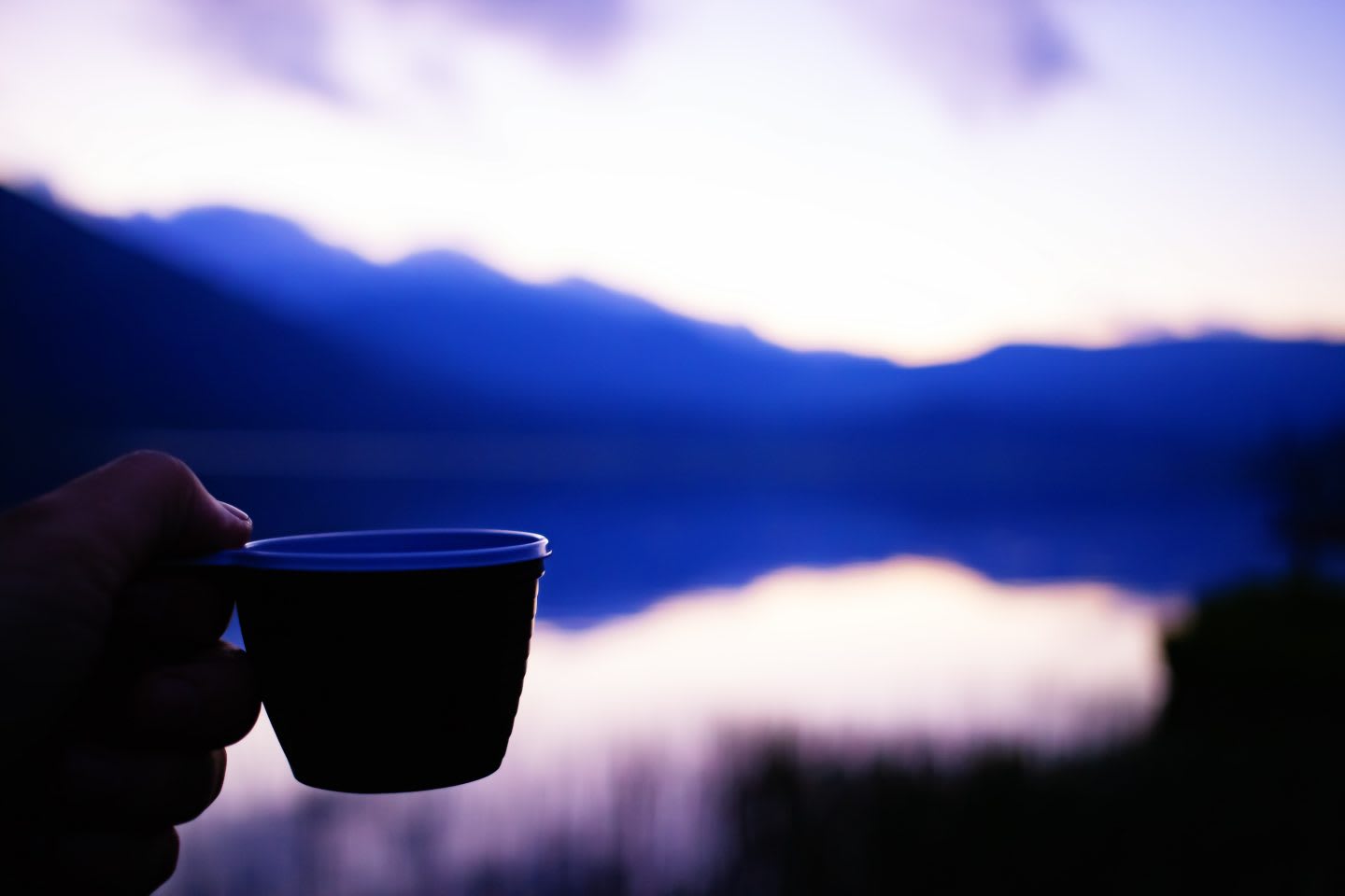 Cup of coffee in the hand of a traveler at sunset in the mountains near the lake. nutrition tips, healthy nutrition, fitness, outdoor, hiking, food, GamePlan A