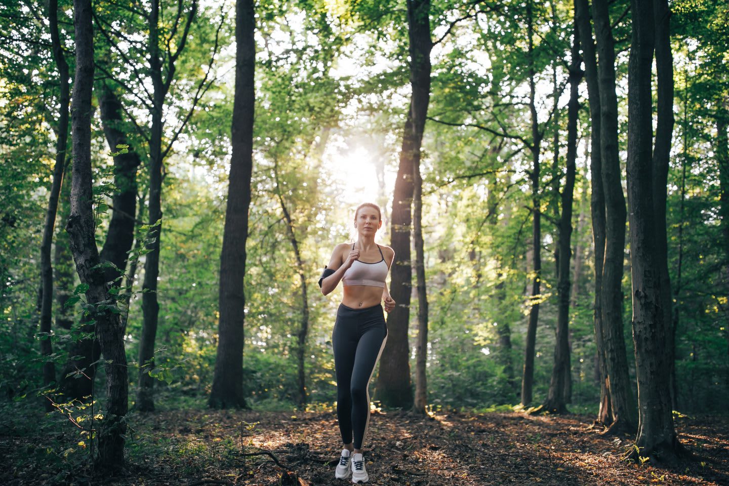 Woman running in a forest with light breaking through trees, morning routine, athletes, running, early morning run, motivation, habits, GamePlan A