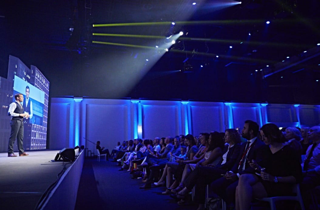 Man presenting on stage in front of large audience, confidence, presentation skills, training, out of your comfortzone, presenting on stage, GamePlan A, boost confidence