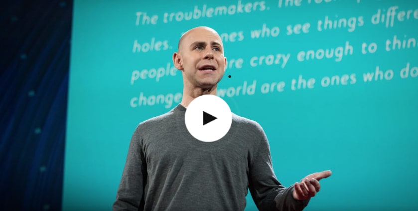 Man in grey shirt gesturing on stage in front of a blue background with words while giving a speech, Adam Grant, TED Talks, headpiece, creativity, talk, GamePlan A