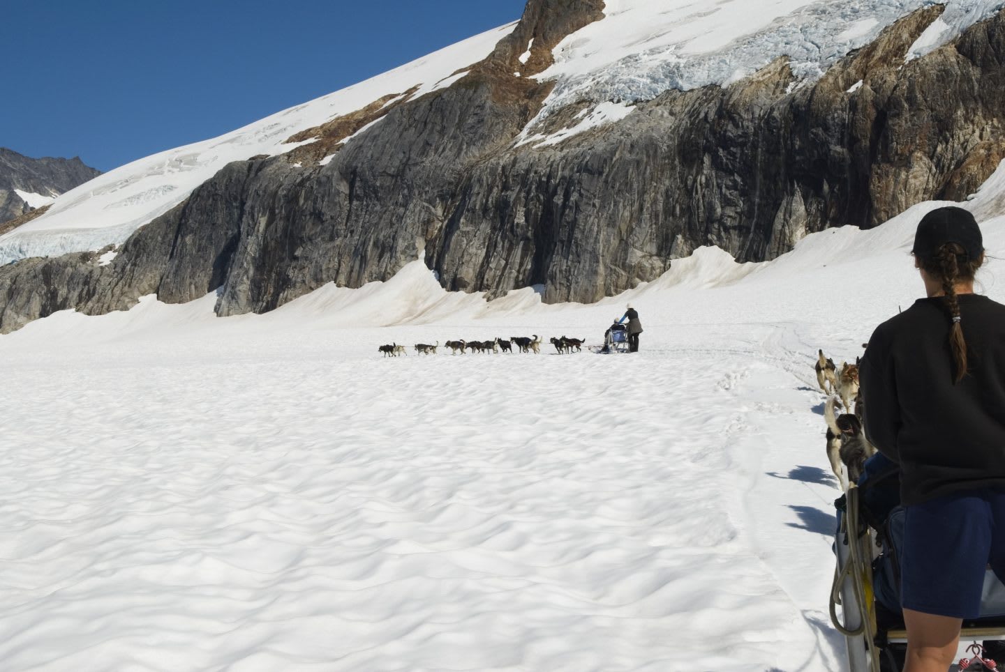 Woman driving a dogsled with another dogsled team on the trail ahead, snow, mountains