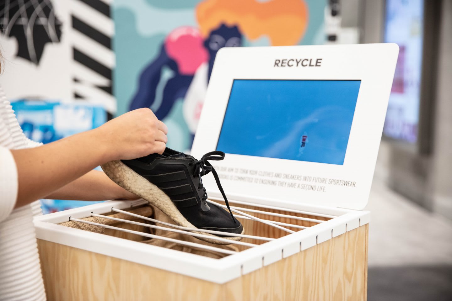 A woman putting an old adidas sneaker in a take back program box. sustainability, recycling, product take back program