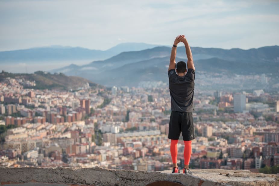 A man standing on a viewpoint looking down on a big city while stretching for a run.