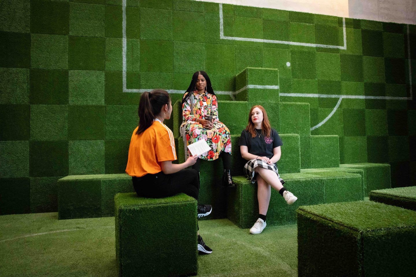 An interview situation in an adidas meeting room, which looks like a football pitch. Three women are chatting with each other. female fan, empowerment, diversity, platform, adidas, football, GamePlan A, SEASON zine