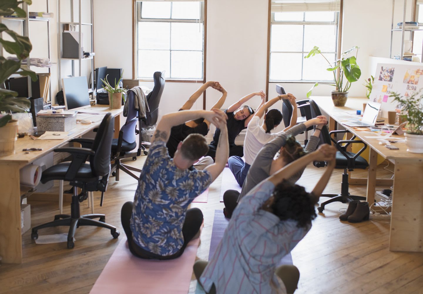 Creative business people stretching, practicing yoga as part of their employers wellness program in the office.