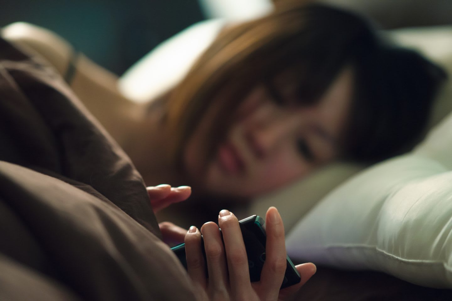 Young woman lying on side in bed operating smartphone | Key to success