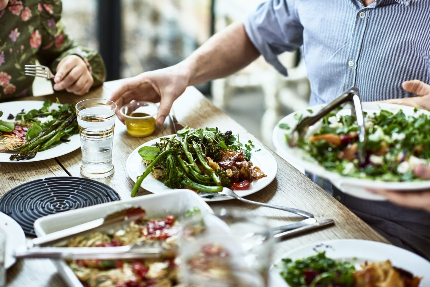 Close up shot of people sitting at dining room table with plates of vegetables and salad, person serving guests at dinner party, man about to pour dressing on his meal, great leader, nutrition, health, fitness, leadership, leadership skills, GamePlan A
