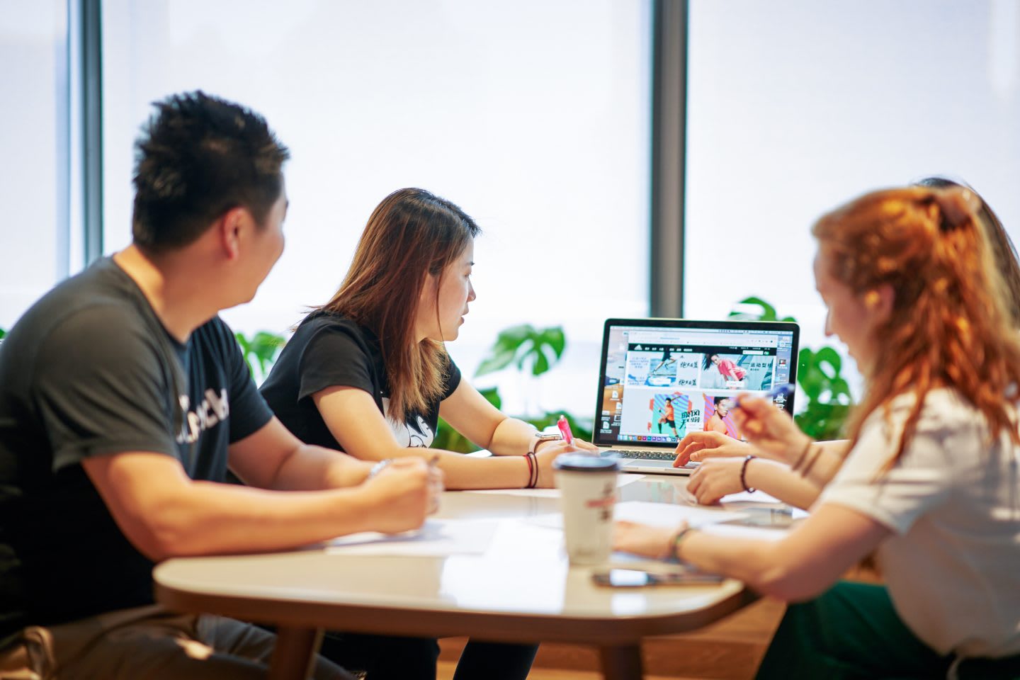 Four people working at the office around a desk in summer.