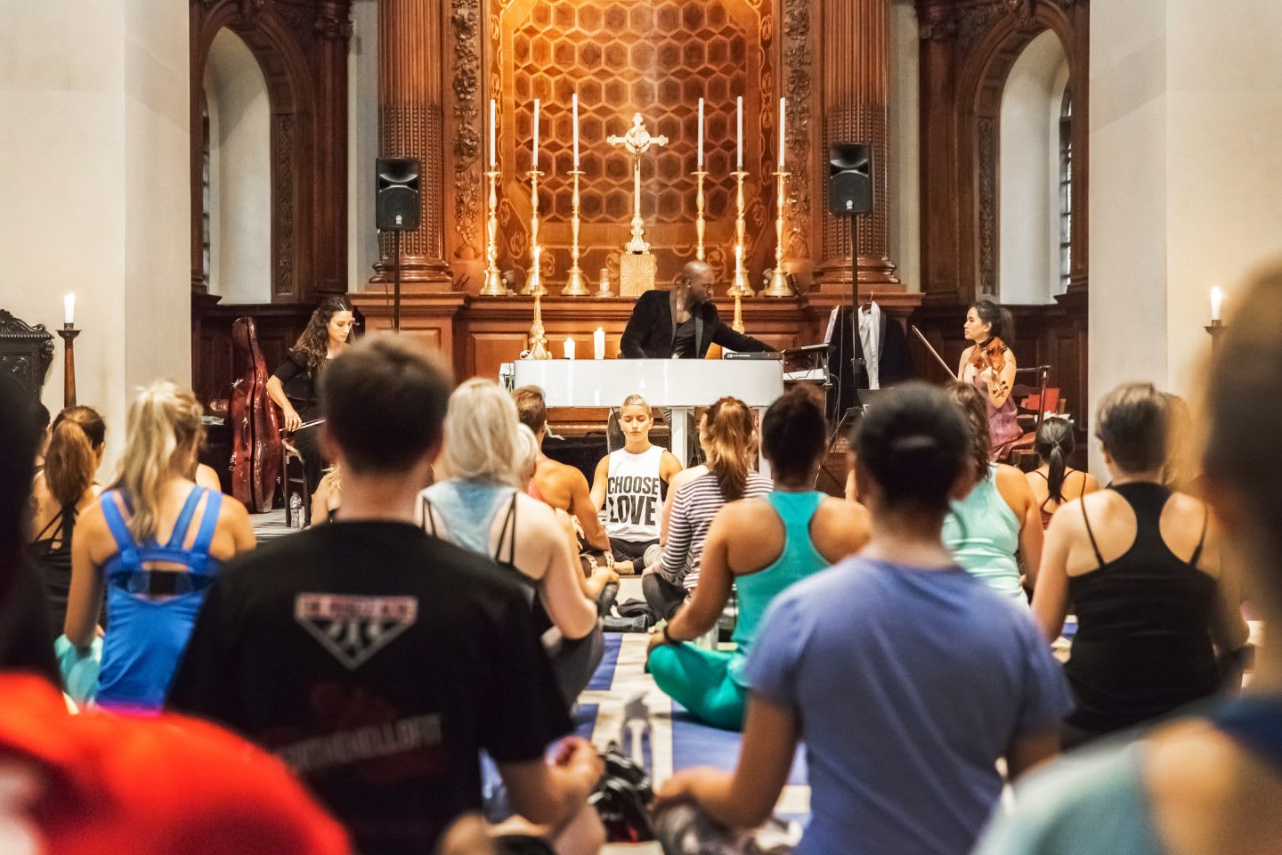 People sit crossed-legged on yoga mats in a beautiful church with a live orchestra playing music. Wellness, Gameplan A.