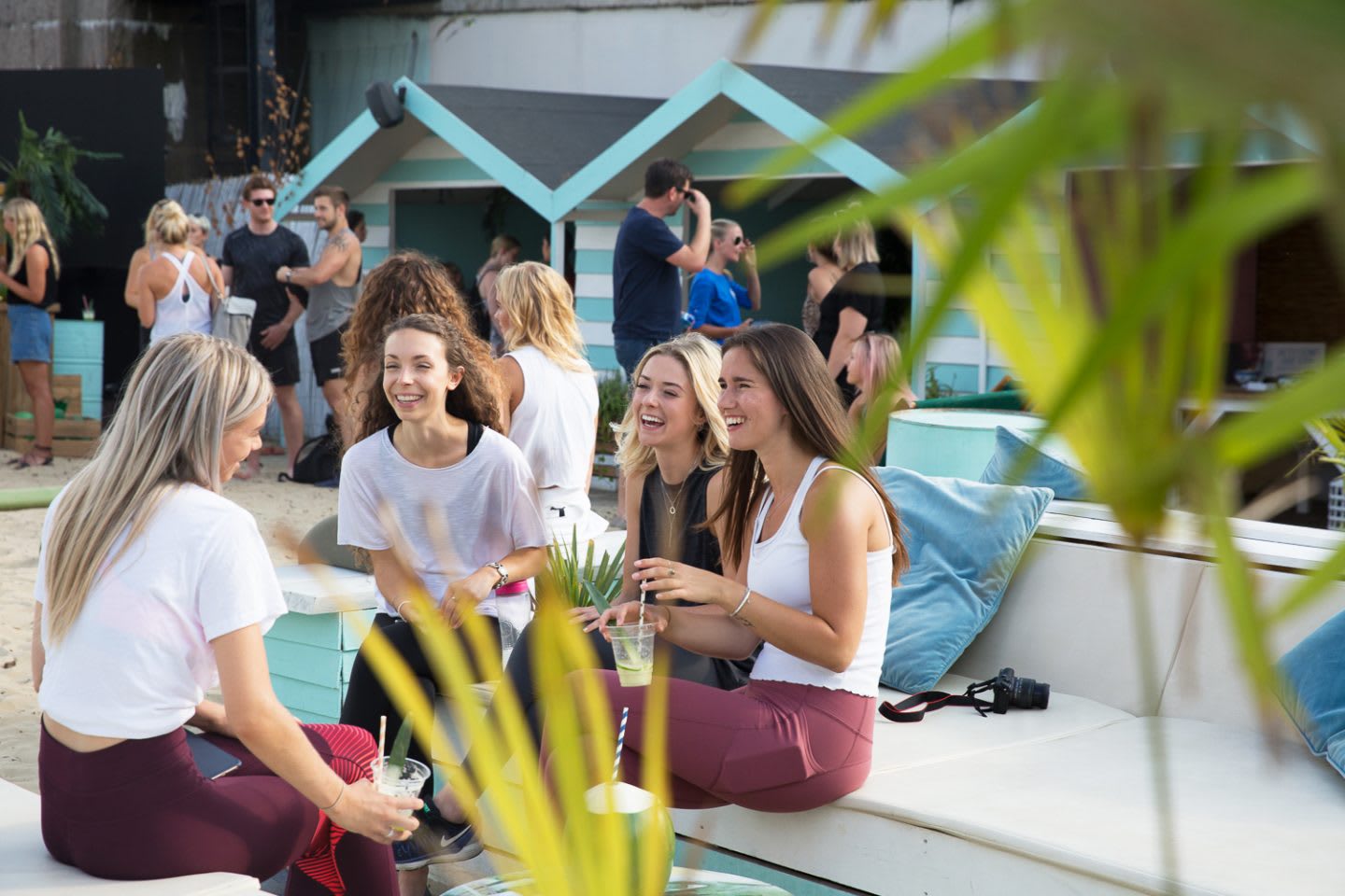 Four young women sit and laugh together on a beach. Wellness, Gameplan A.