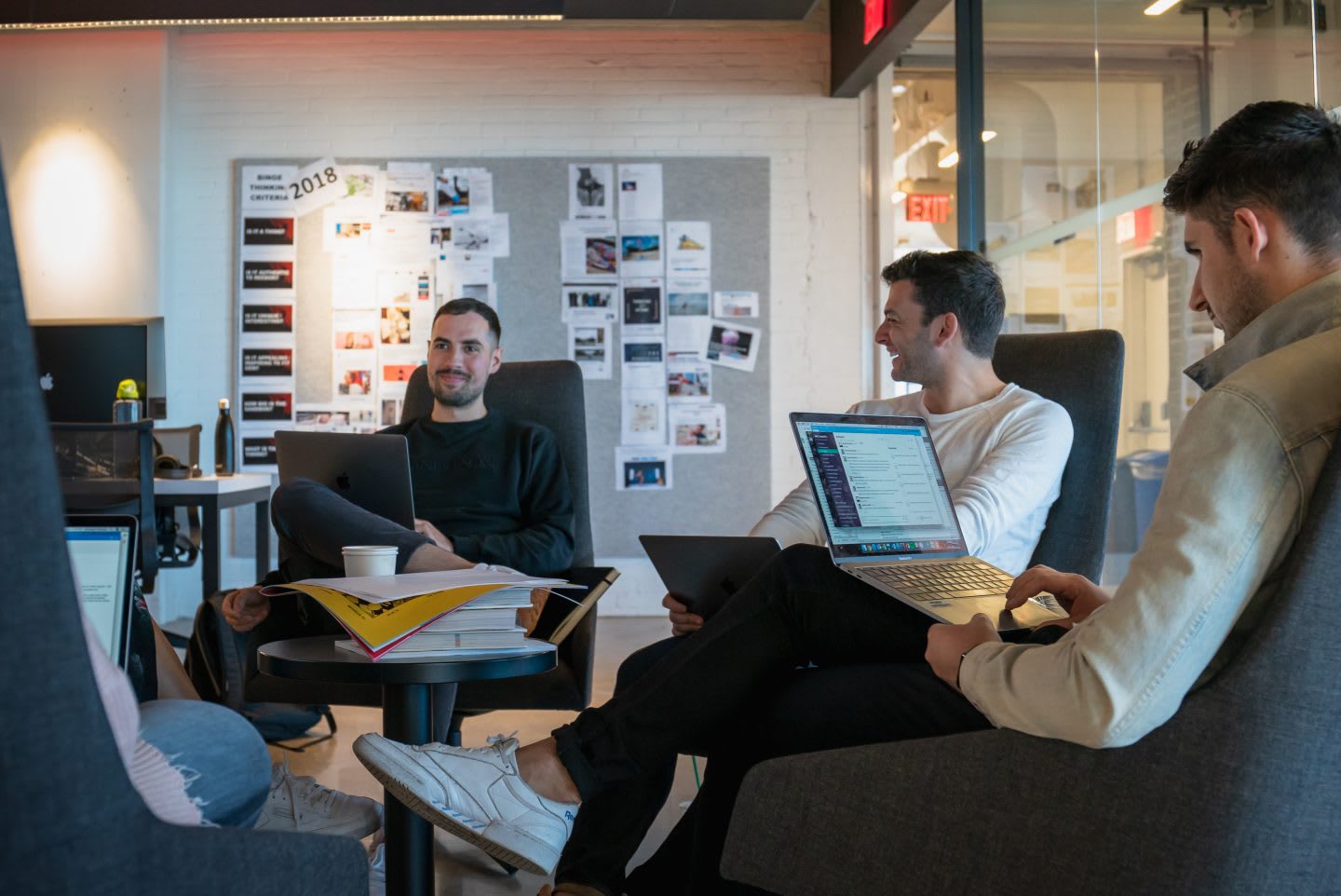 A group of colleagues sit with their laptops in a relaxed meeting environment.