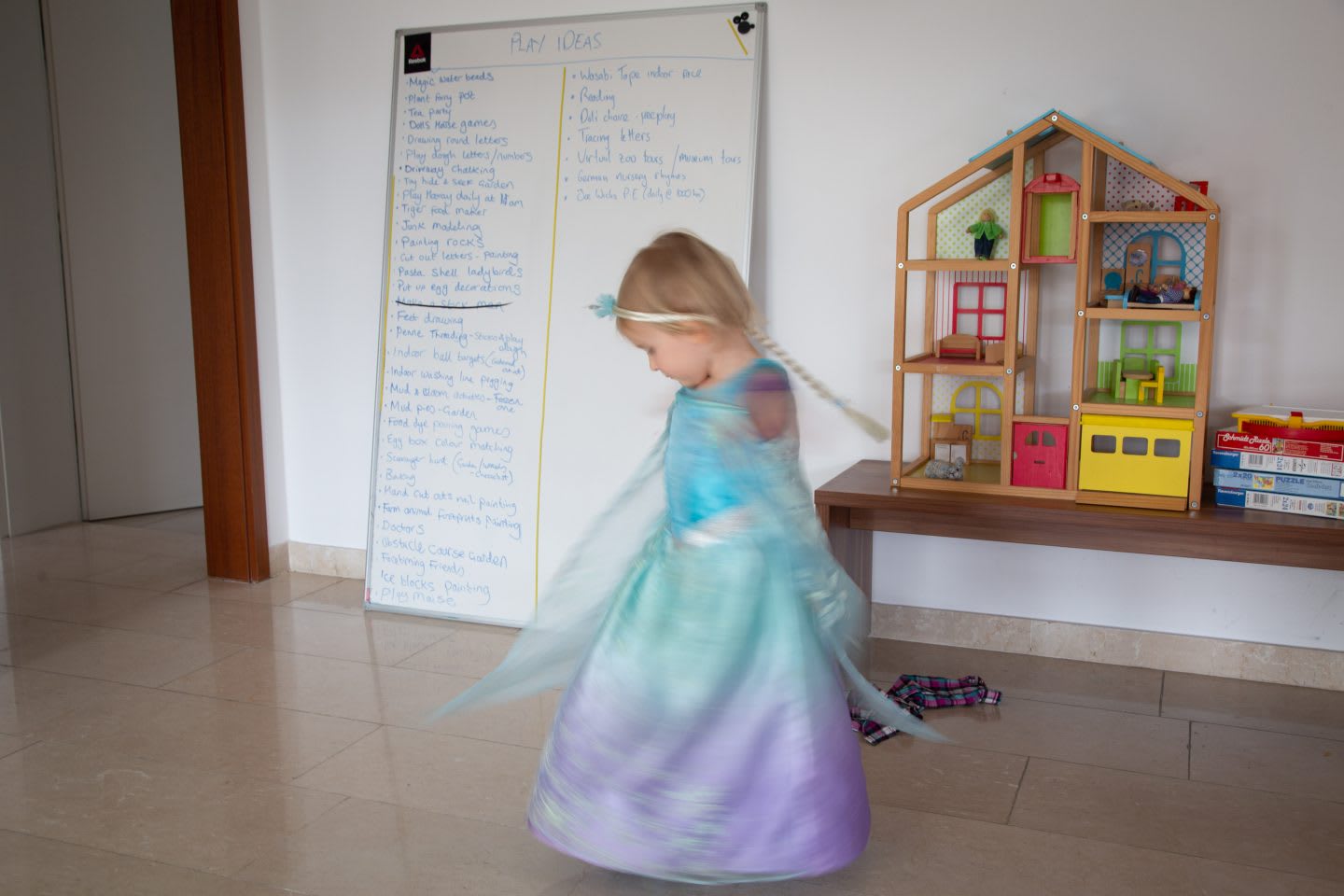 Girl dancing at home in princess costume and a whiteboard that shows a list of play ideas in background. working from home with kids. Habits and routines, Parenting, coronavirus.