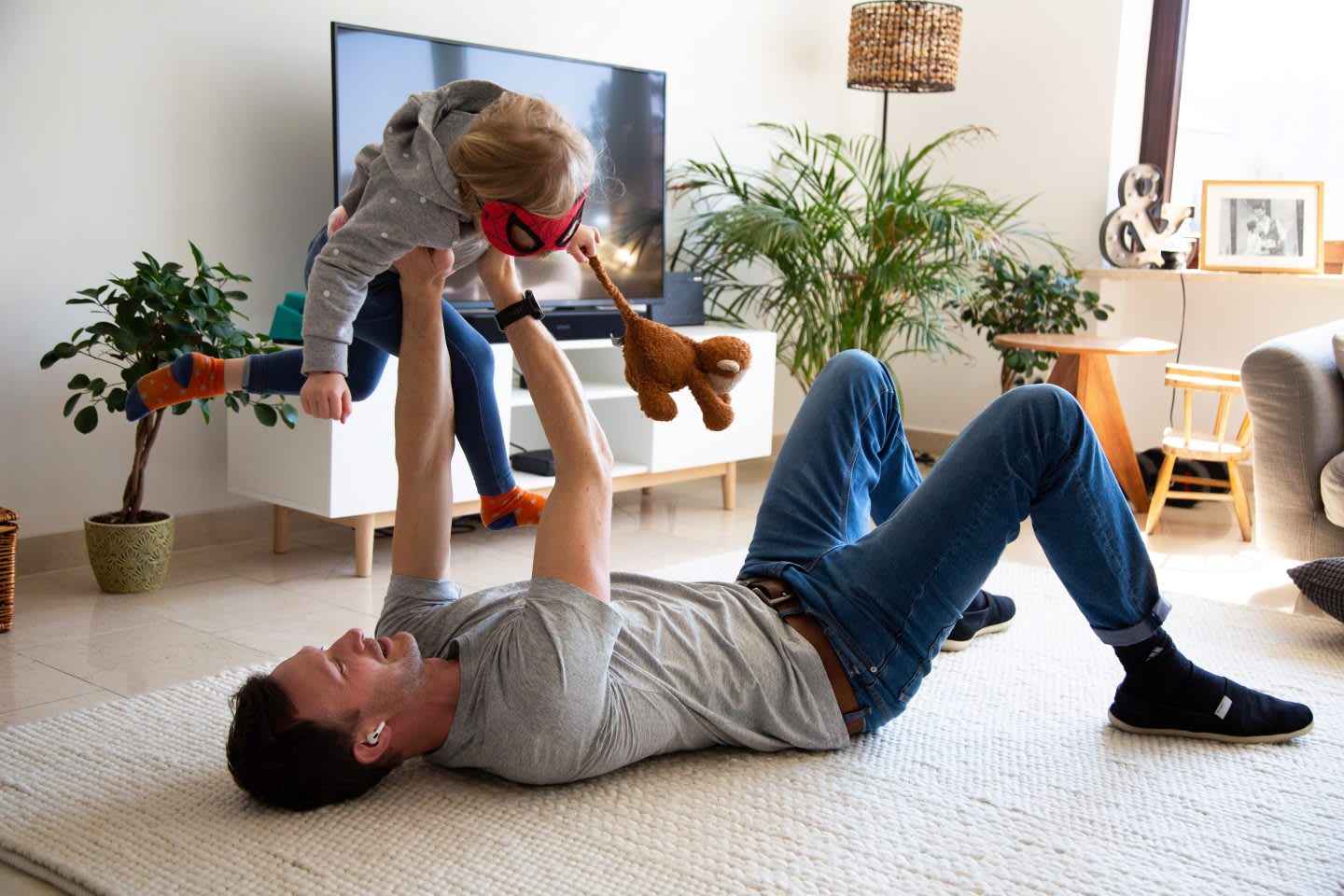 Dad laying on carpet holding daughter in the air at home while in conference call. working from home with kids. Habits and routines, Parenting, coronavirus.
