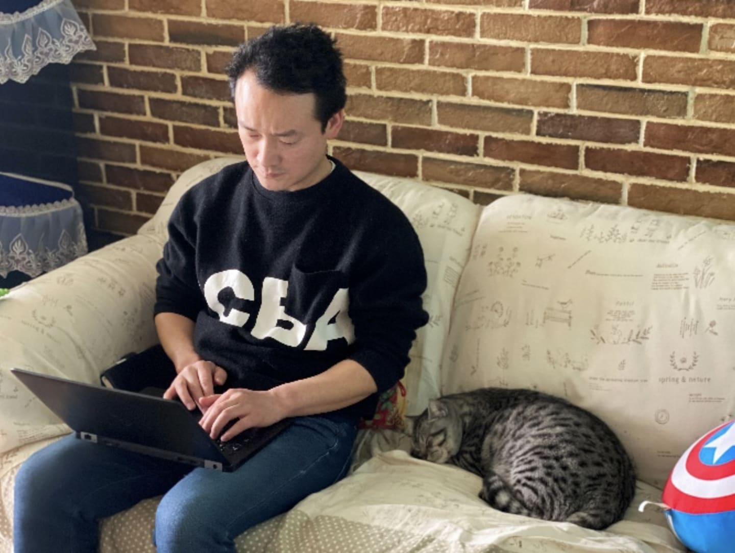 Man working from home on laptop next to pet cat, work from home, remote working, home office, China, Wuhan, coronavirus