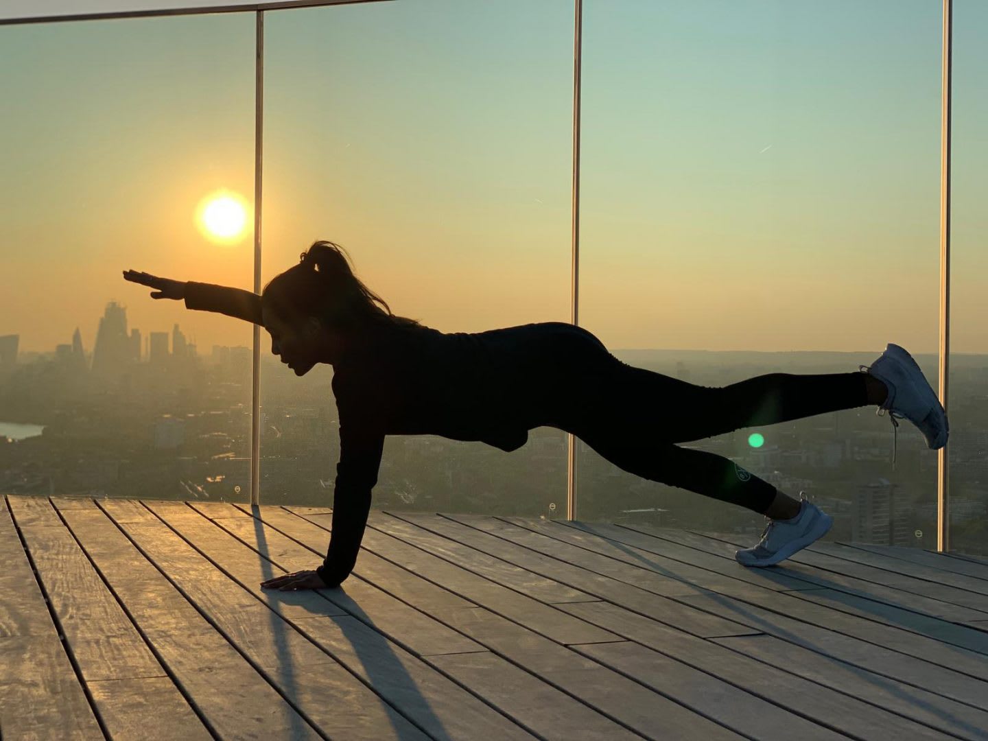 A women planking in an apartment while the sun rises over the skyline. Wellbeing, habits and routines, health, mental strength, healthy lifestyle, GamePlanA