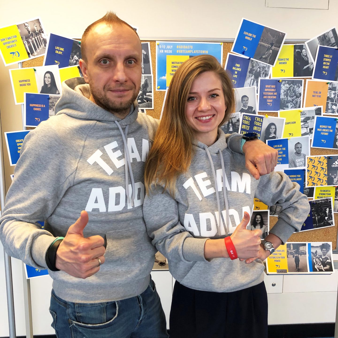 Man and woman wearing grey sweatshirts smiling with thumbs up gesture, teamwork, team, collaboration, happiness, workplace, worklife, culture, adidas
