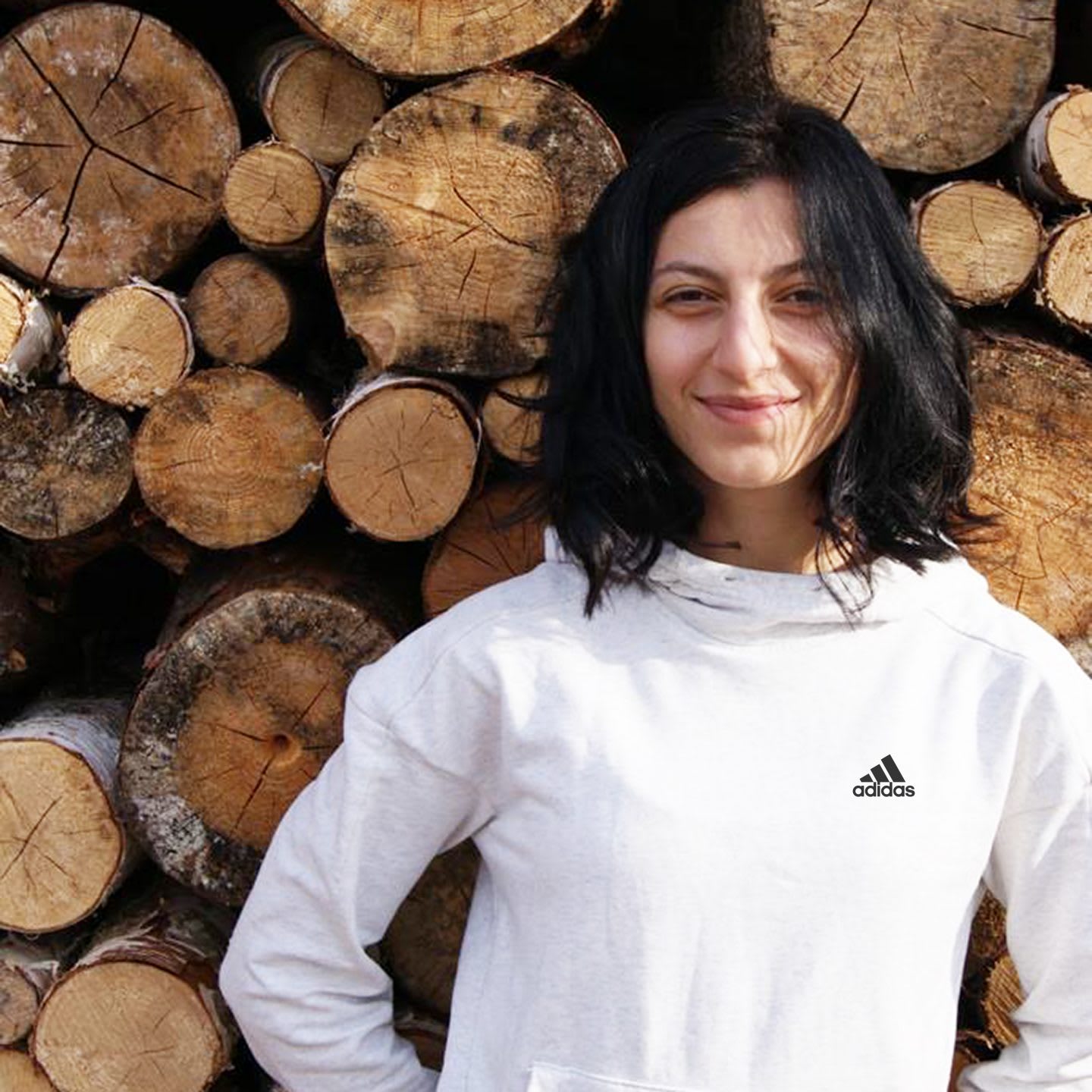 Woman with dark hair wearing adidas sports clothes smiling in front of logs, woman, girl, employee, adidas, sports