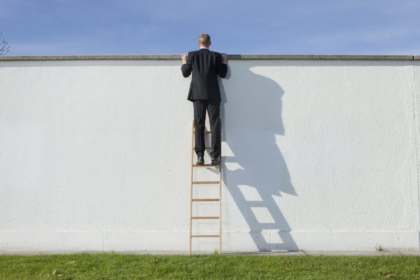 Businessman on ladder looking over wall, curiosity, confidence, unknown, risk, bravery