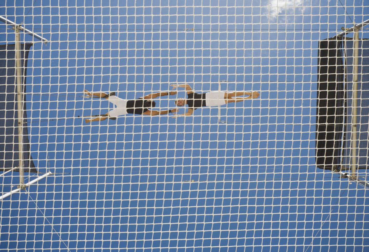 Male trapeze artist catching man, low angle view, acrobat, risk, sky, net, tricks
