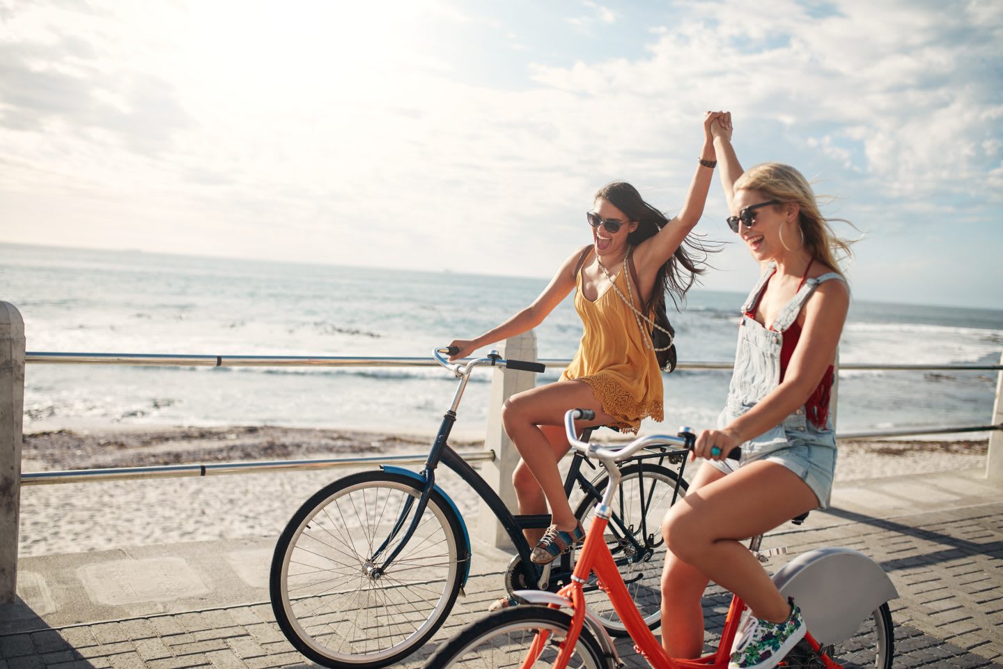Female friends enjoying cycling on a summer day. Two young female friends riding their bicycles on the seaside promenade, cycling, biking, cyclists, fun