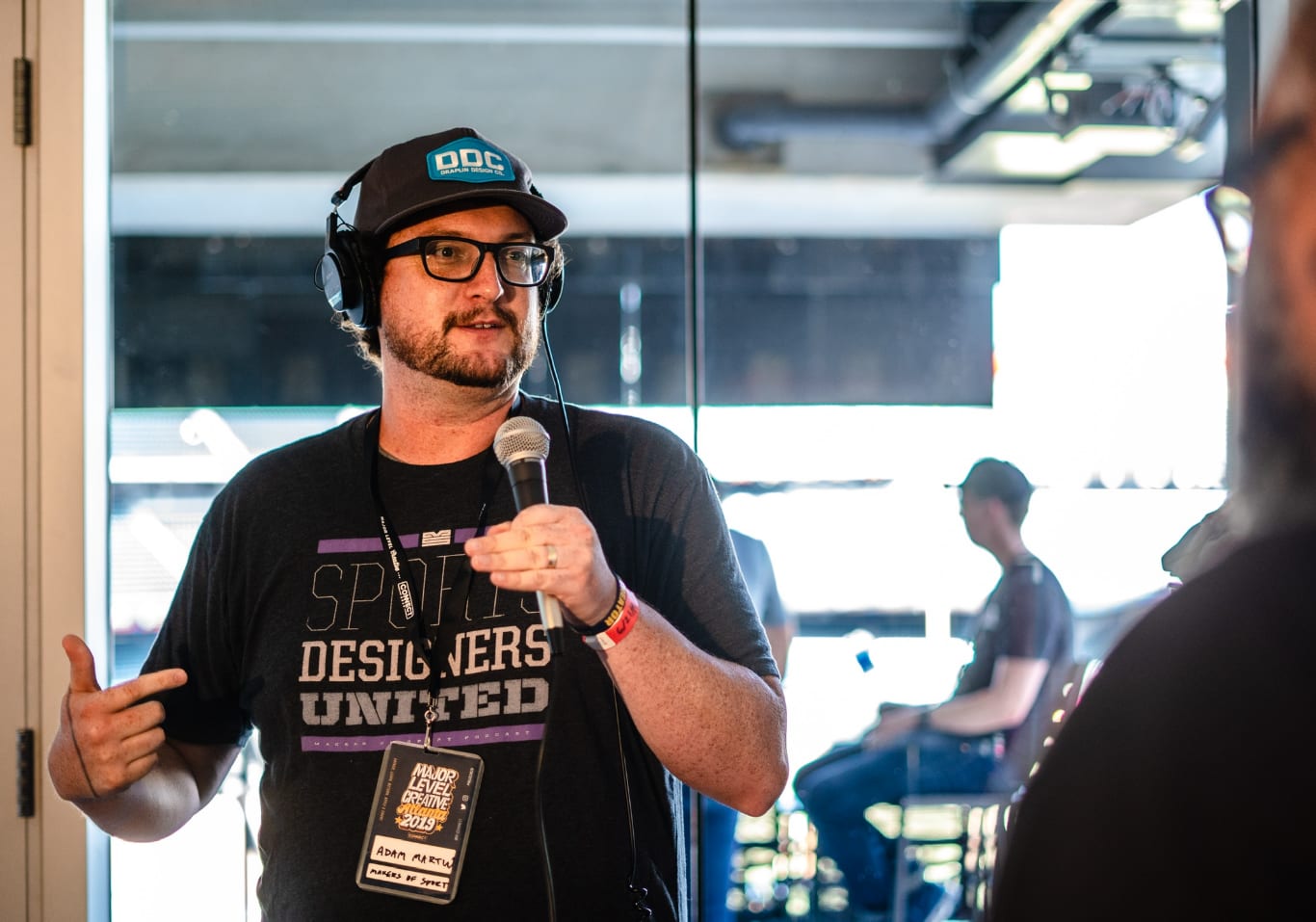 Man wearing glasses holding a microphone in a recording studio with headphones, Adam Martin, Makers of Sport, studio, recording, podcast, listening