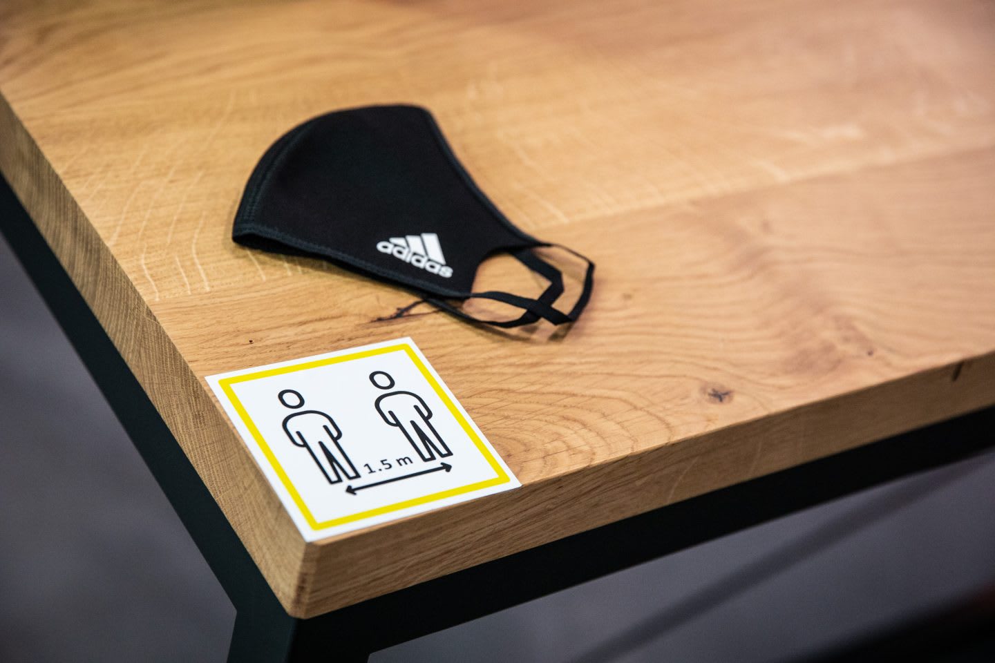 Black face mask with white adidas logo on wooden table with safety measures sign for COVID-19 outbreak, adidas, HQ, headquarters, precaution, health, employees, campus, Herzogenaurach