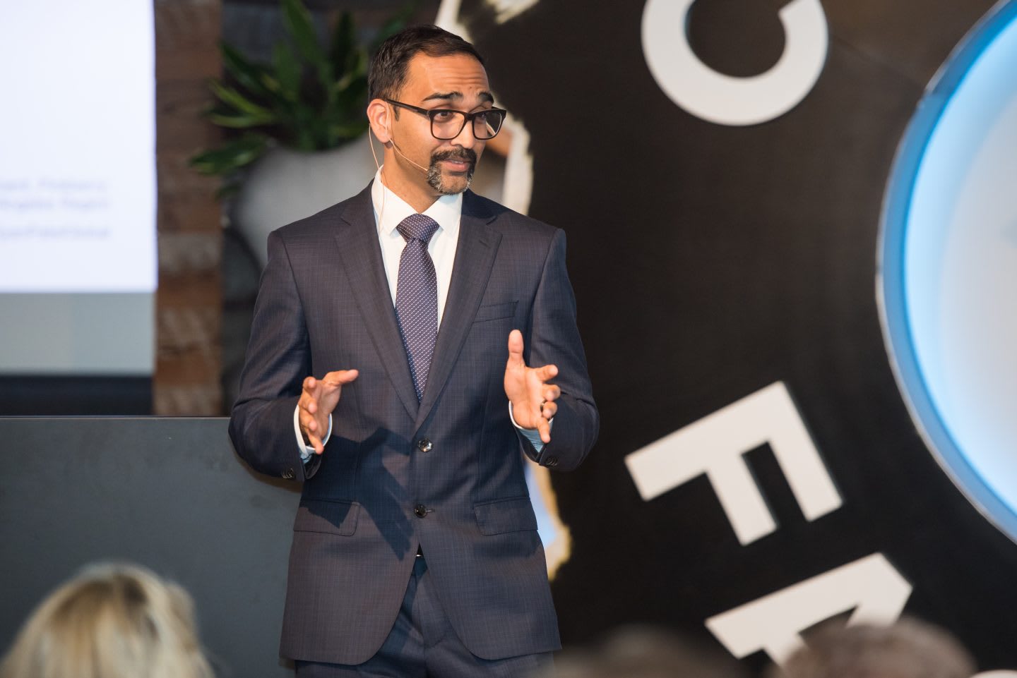 Man wearing a suit and tie giving a presentation on stage, Ryan Patel, public speaking, speech, business, expert, conference