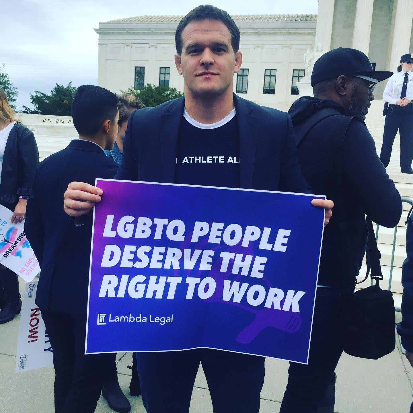 Man wearing dark suit holding up sign in support of LGBTQ people, Hudson Taylor, founder, Athlete Ally, LGBTQ, inclusion, diversity, protest