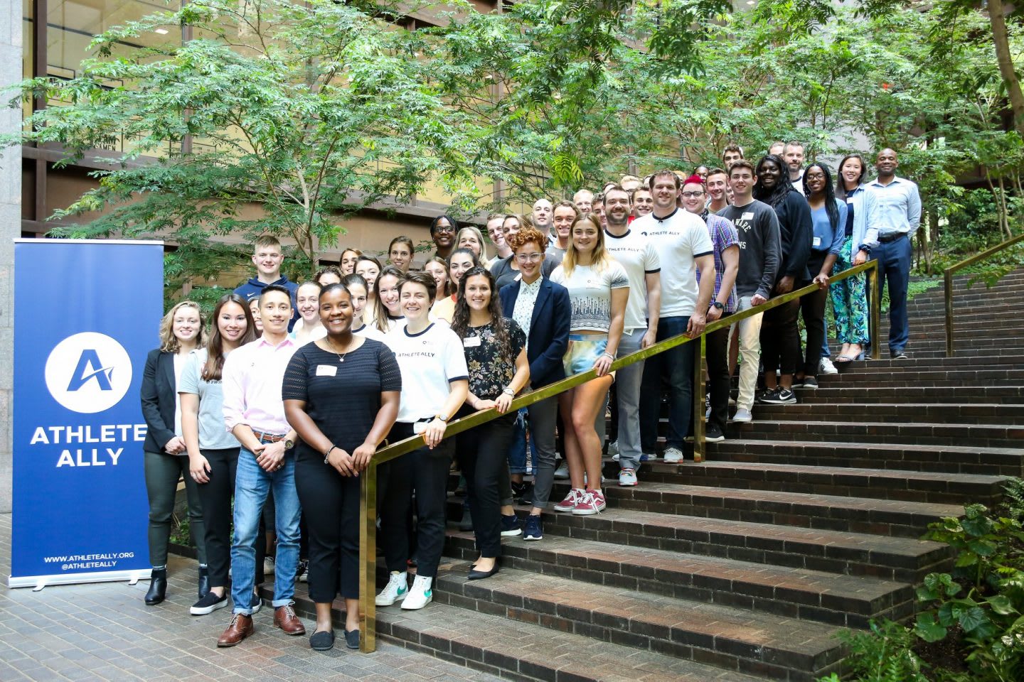 Men and women standing on steps in front of Athlete Ally sign, students, summit, conference, LGBTQ