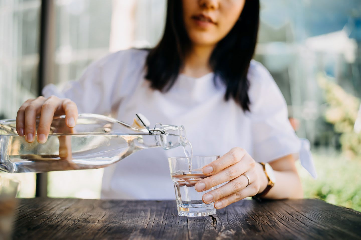 Woman pouring water from bottle into the glass at a outdoor cafe, hydration, water, healthy, diet