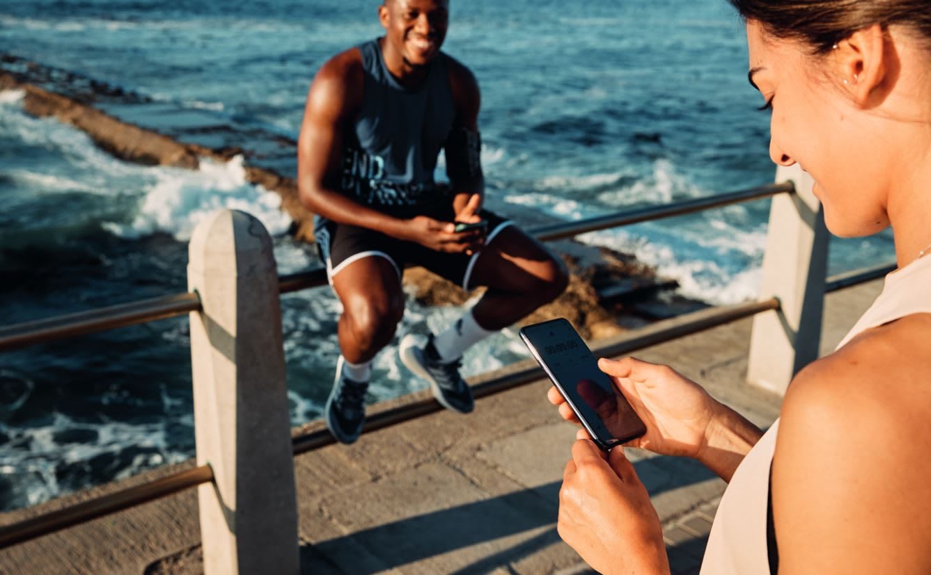Woman looking at mobile phone by ocean, adidas, sports, fitness, running, Run For The Oceans, sustainability, plastic, waste, event, GamePlan A