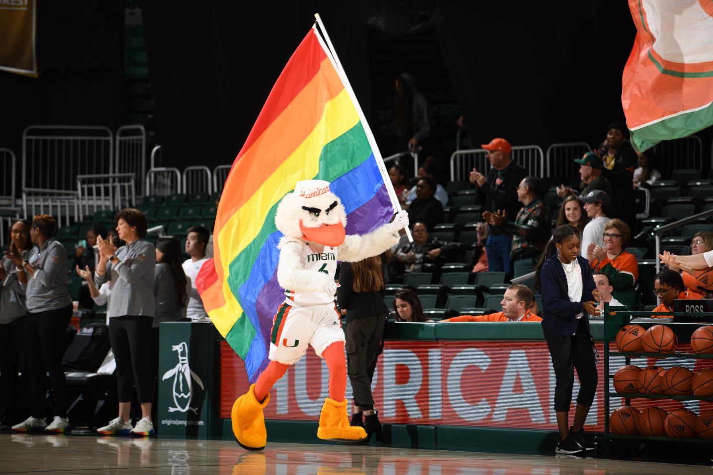 The mascot of the Miami Hurricanes Women Basketball Team holding a Pride flag while running through the stadium. Pride, LGBTQ+, Athletes, Sports, Equality, GamePlan A.