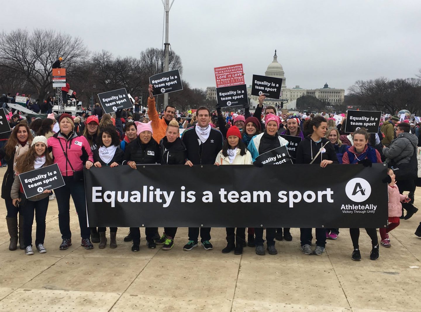 A group of people standing in front of the US Capitol holding a sign together which says: