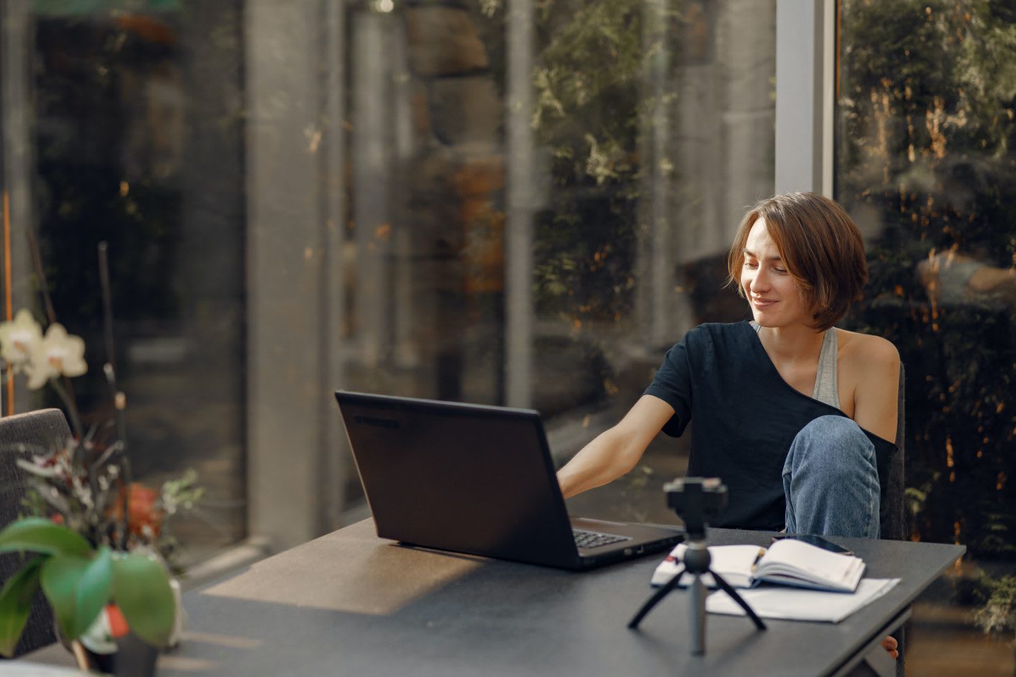 Woman sitting on a desk next to a window working on a laptop. Virtual meetings, work remotely, home office