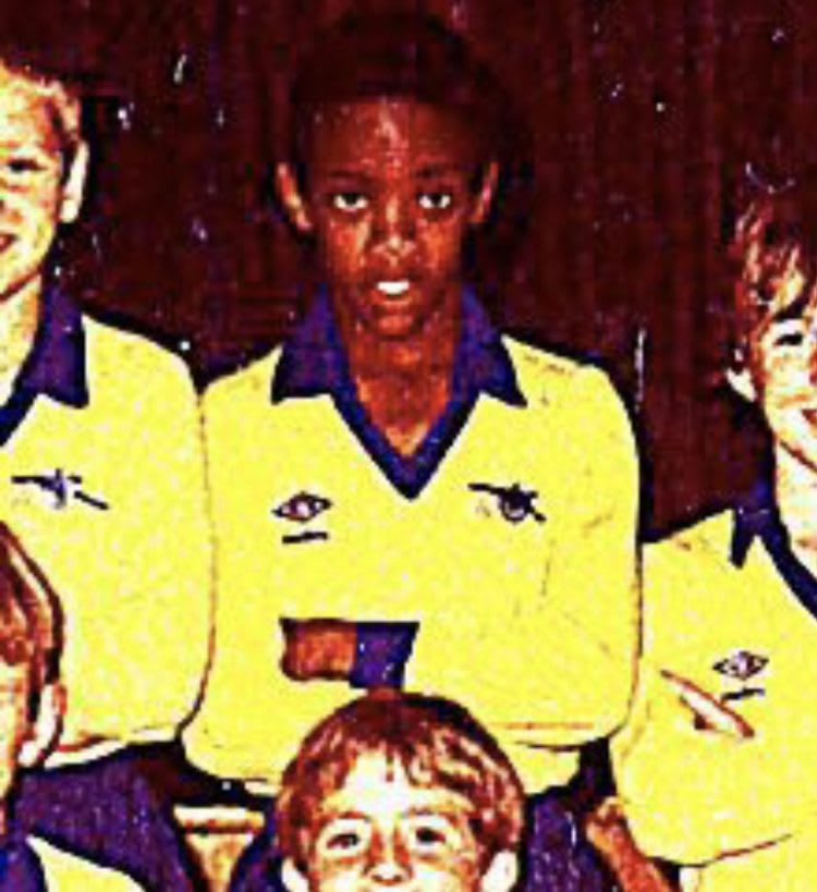 Child in yellow sports jersey as member of a team, dark background, arms crossed