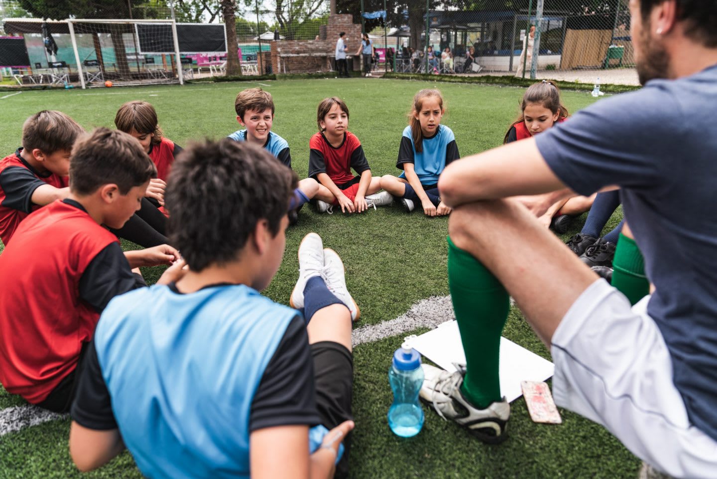 Coach explaining the strategy for the soccer competition to a team of kids sitting in circle