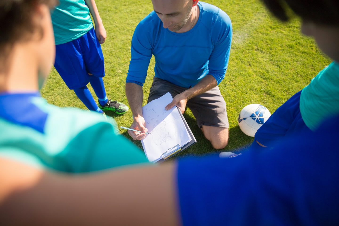 Football coach showing a huddle of young players a play.