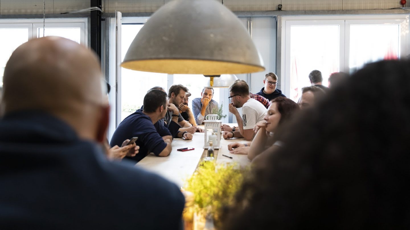 A group of workers gather together to discuss topics in a busy work setting.