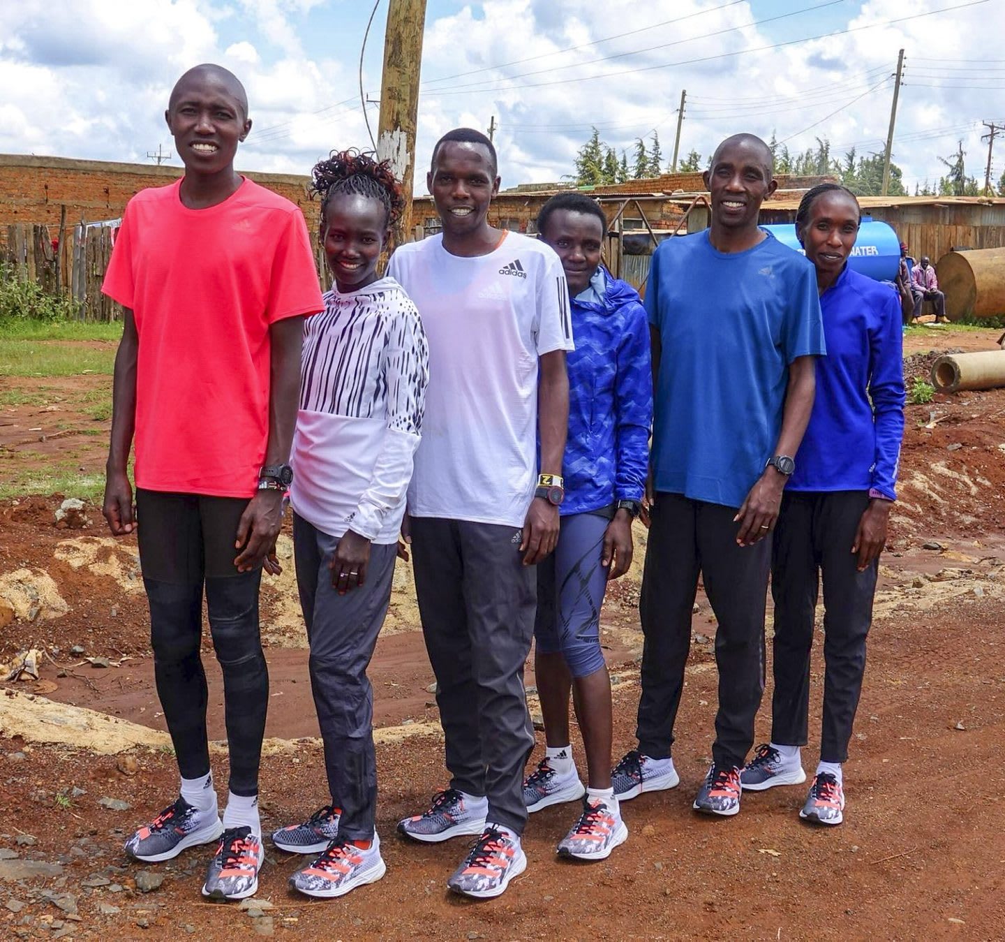 A group of Kenyan athletes stand in a group with a adidas running shoes on their feed in a training session.