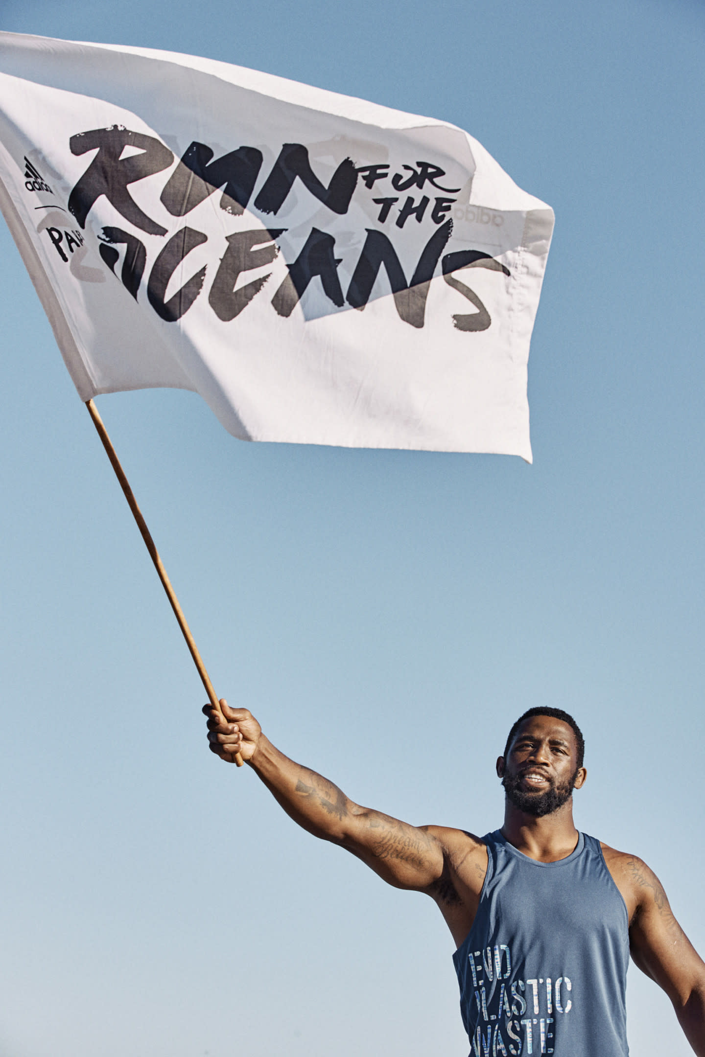 Siya Kolisi holds and waves a Run for the Oceans flag against a blue sky.