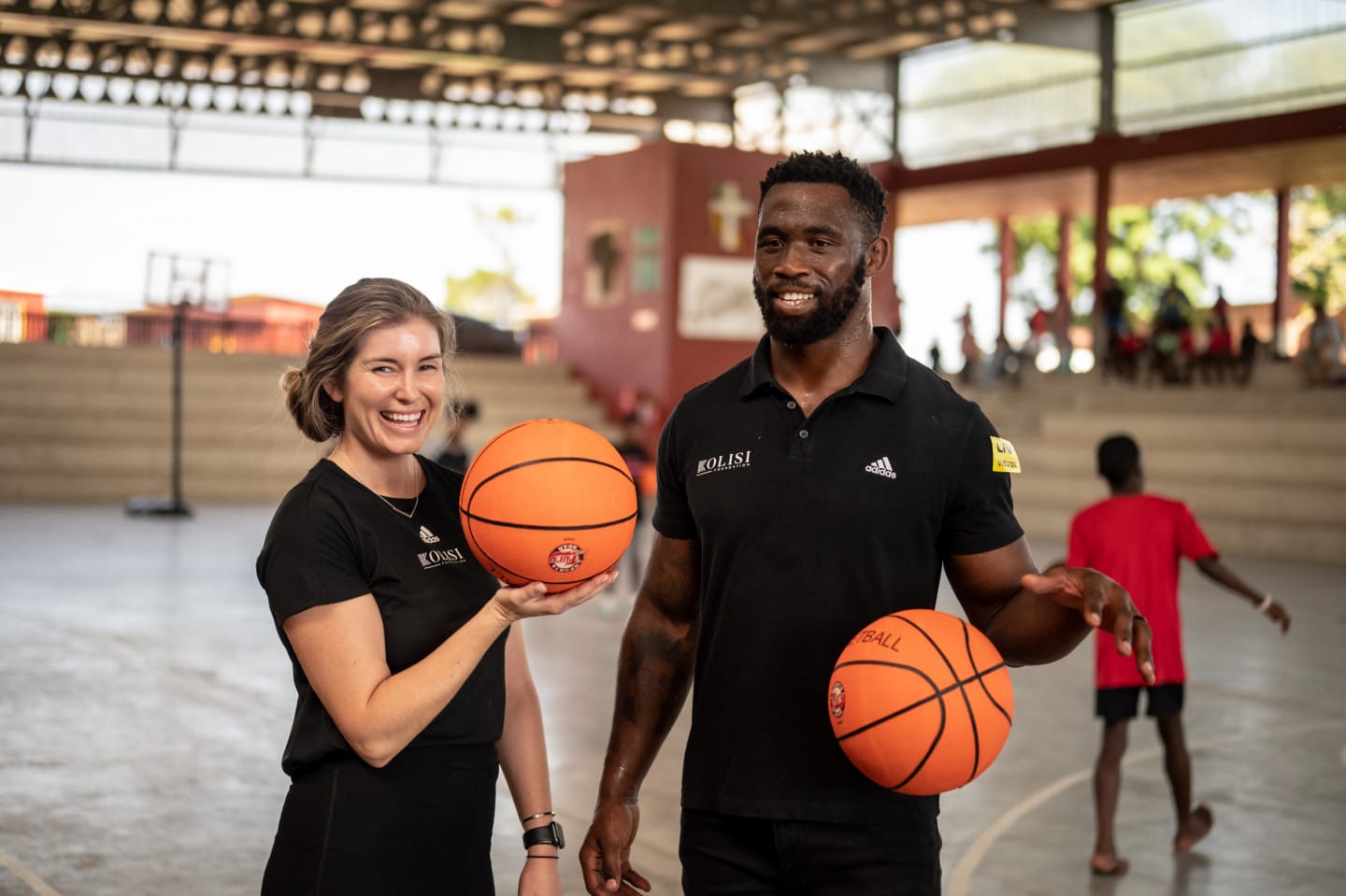 Siya Kolisi and Rachel Kolisi stand next to each other holding two basketballs ready for a game.