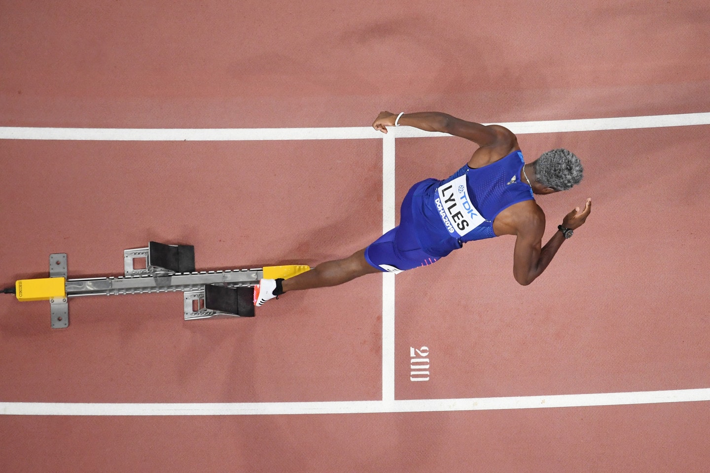 Noah Lyles getting ready to sprint on a track wearing adidas shoes