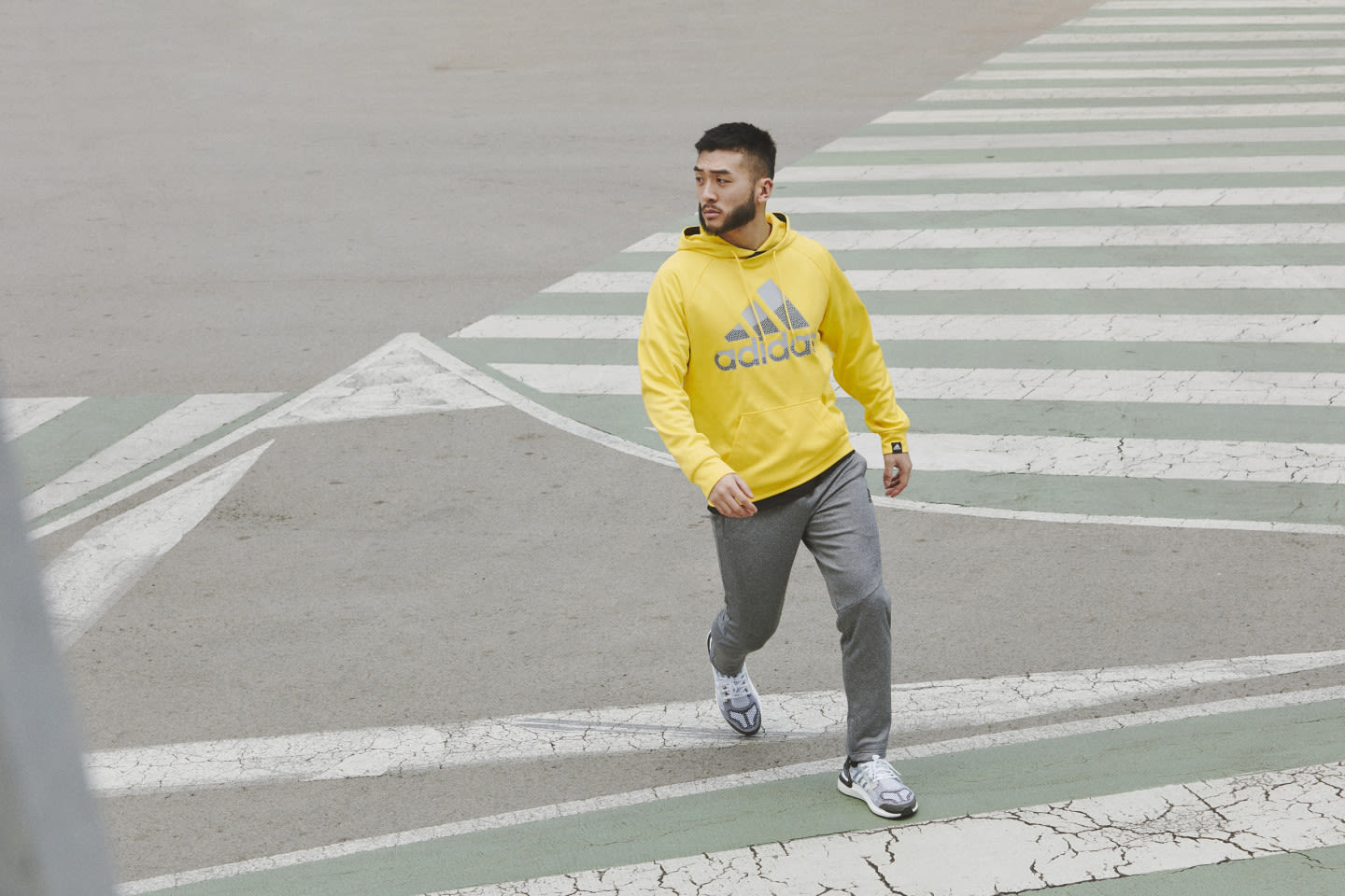 Man walking on a sidewalk wearing a yellow adidas hoodie